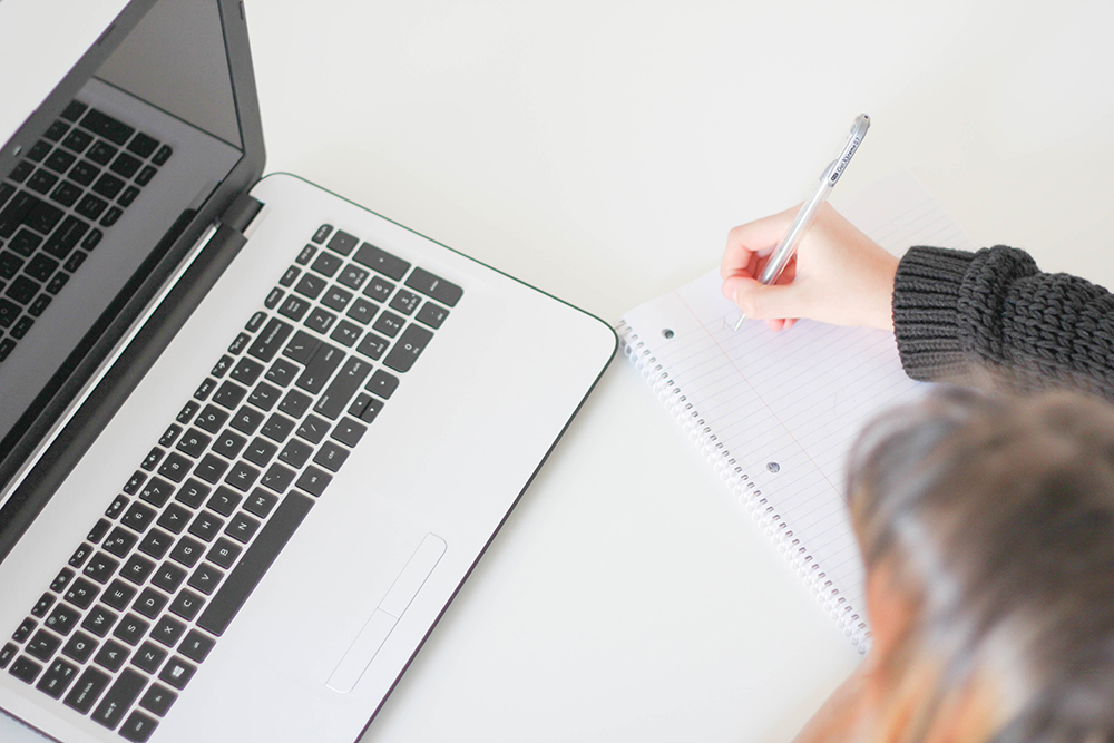 Student taking notes next to a laptop