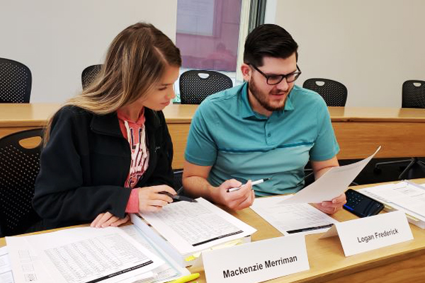 Two students at a desk look a piece of paper. 