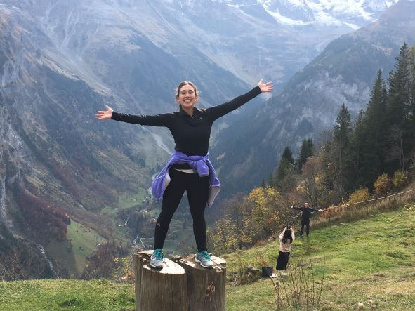 Female stands on rock in front of mountains with arms up. 