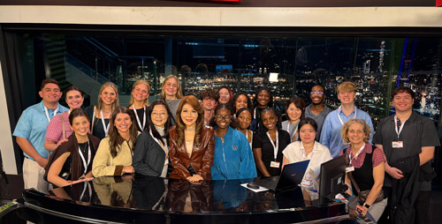LSU business students and faculty members crowd around a news desk to pose with a Taiwanese media personality. The group is dressed in business attire and smiles at the camera.