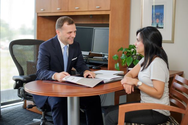 Man in suit talks with female student in office. 