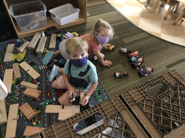 young boy and girl wearing masks play with blocks and figure