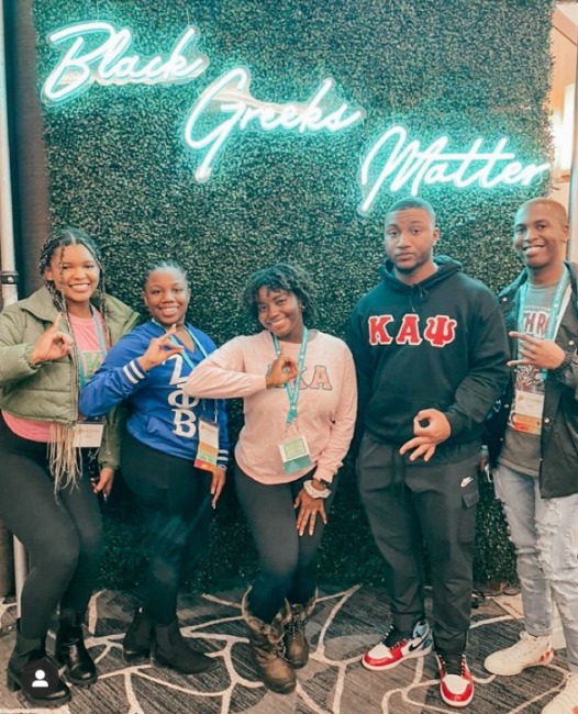 members in front of black greeks matter sign